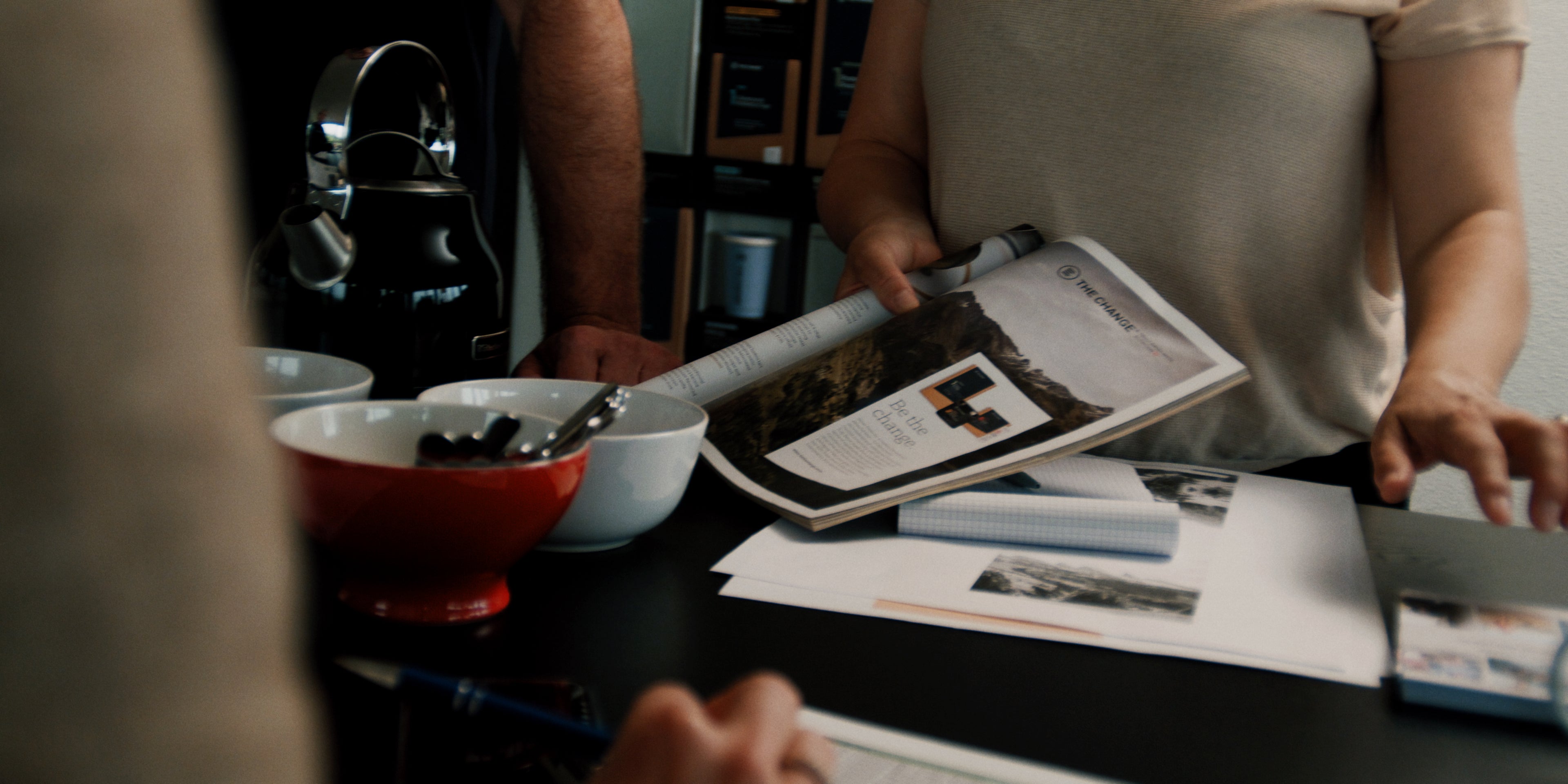 A modern workspace with a black kettle, red bowl, and magazine on a black table, featuring creative design materials.
