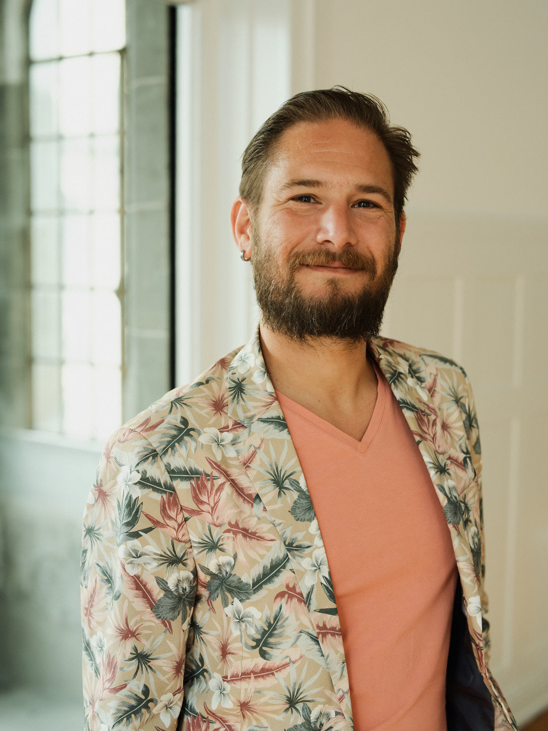 Men's tropical floral blazer in pastel colors over a coral v-neck tee, perfect for stylish summer outings.