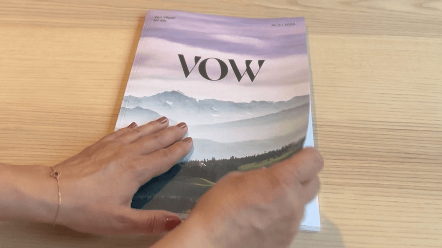 Colorful VOW magazine with a mountain landscape cover, held by a hand with nail polish, showcasing artistic design.